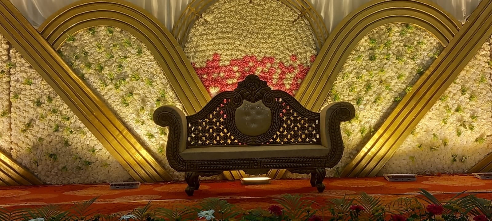 Close-up of the carved stage sofa against a wall of flowers